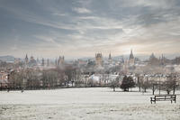 Photo of Oxford's Spires in the snow taken from South Park with a bench in the foreground 